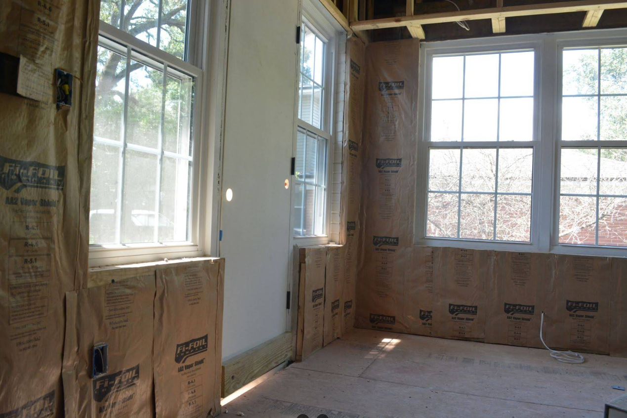 Interior room under construction with windows, insulation, and unfinished walls.