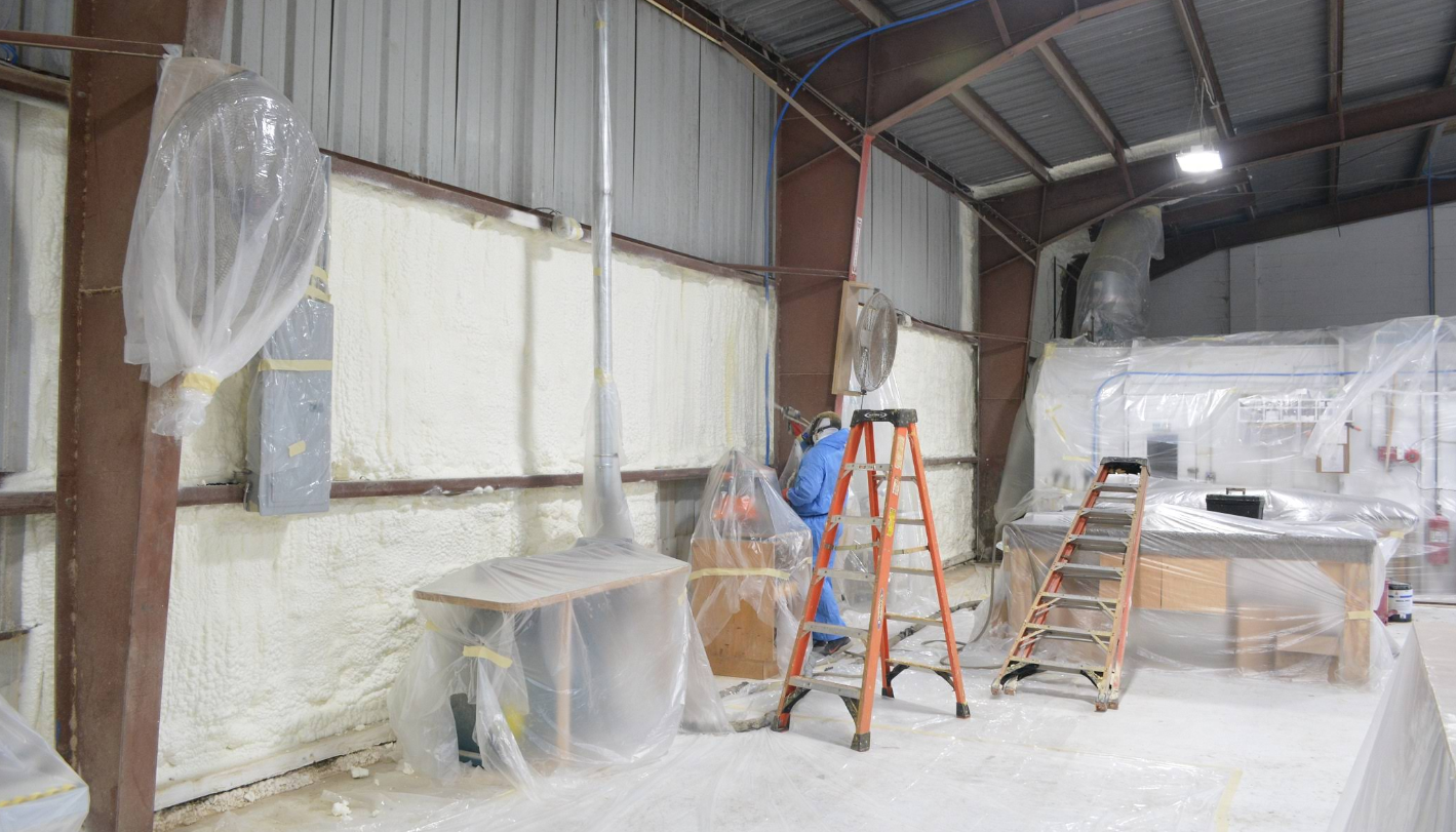 Interior view of a workshop with walls covered in insulation. Ladders and covered equipment are present.