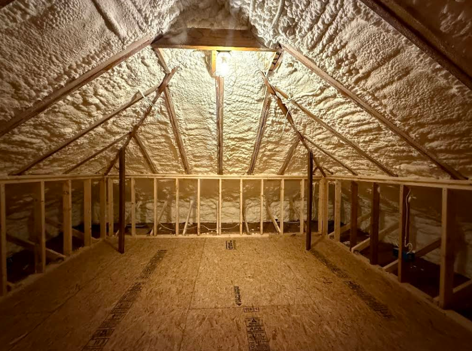 Interior view of a workshop with walls covered in insulation. Ladders and covered equipment are present.