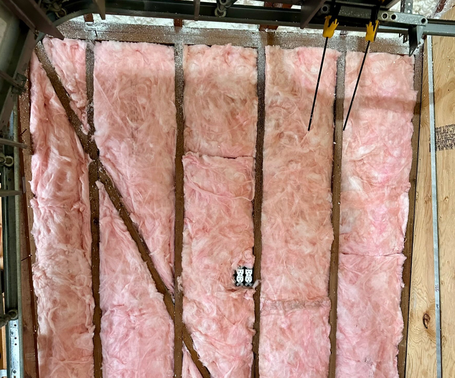 Person installing pink fiberglass insulation in a wooden wall frame.
