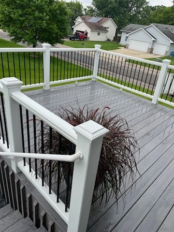 A deck with a white railing and a potted plant on it.