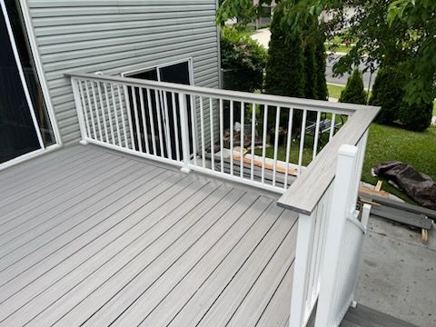 A gray deck with a white railing and stairs is sitting next to a house.