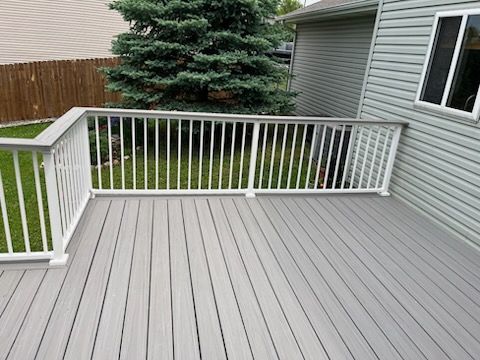 A gray deck with a white railing and a house in the background.