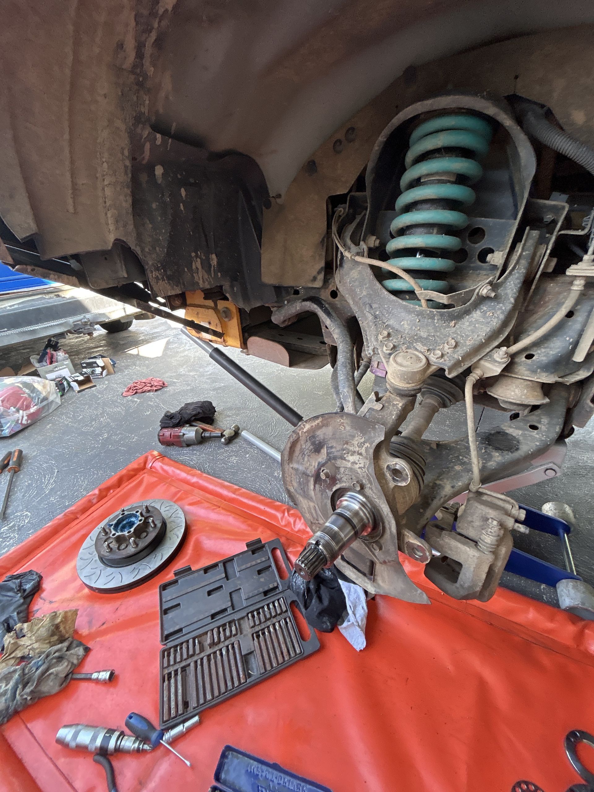 Car wheel suspension disassembled, green coil spring, rotor, and tools on red tarp. — All Auto & Mechanical in The Entrance North, NSW