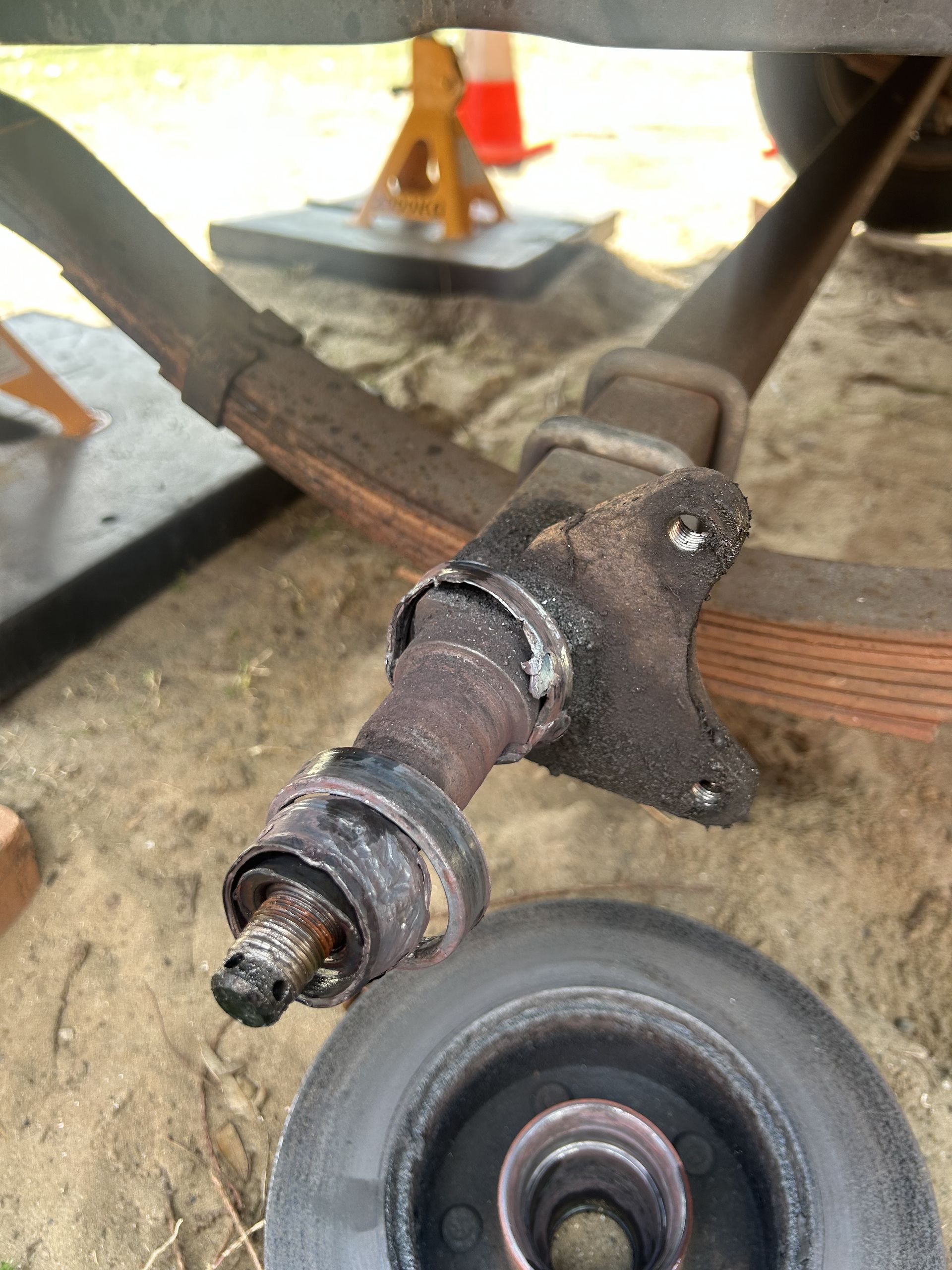 Damaged trailer axle, wheel removed. Rust and welding visible, supported by jack stands in outdoor setting. — All Auto & Mechanical in Erina, NSW