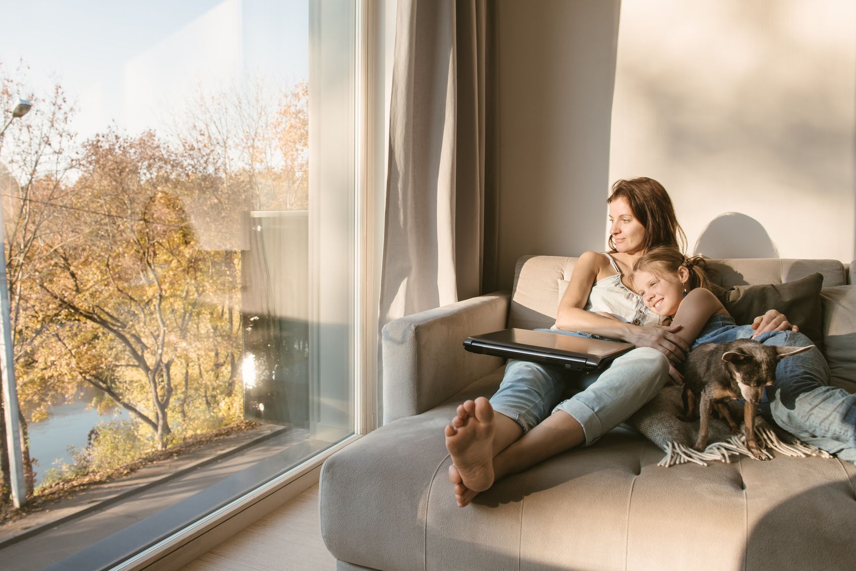 A woman and child are sitting on a couch with a dog.