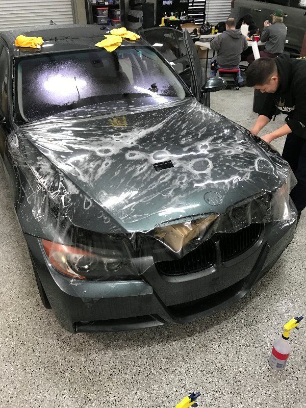 A man is wrapping a car in plastic in a garage.