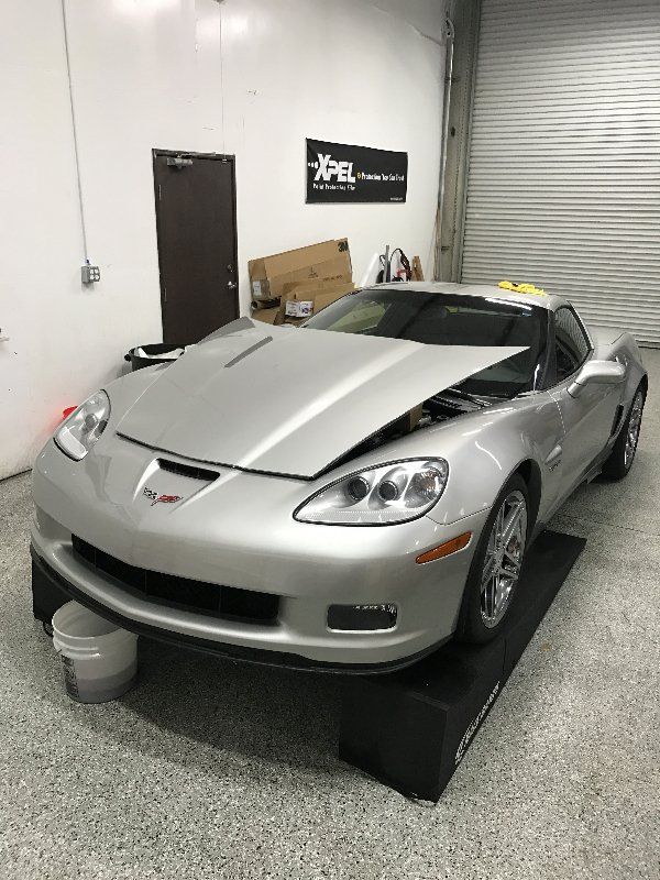 A silver corvette is parked in a garage with its hood up.