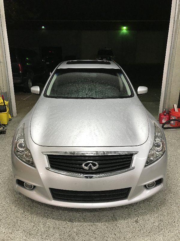 A silver infiniti g37 is parked in a garage at night.