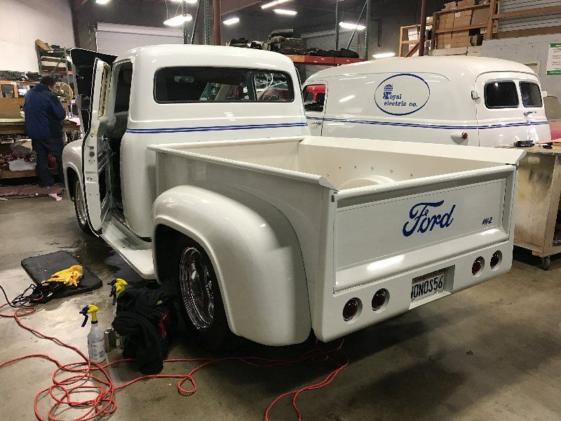 A white ford truck is parked in a garage next to a white van.