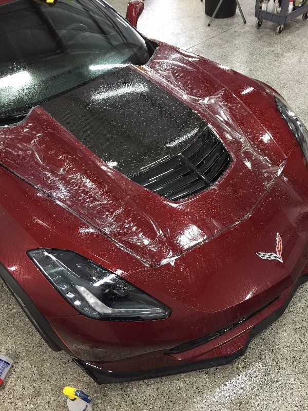 A red corvette is wrapped in plastic in a garage