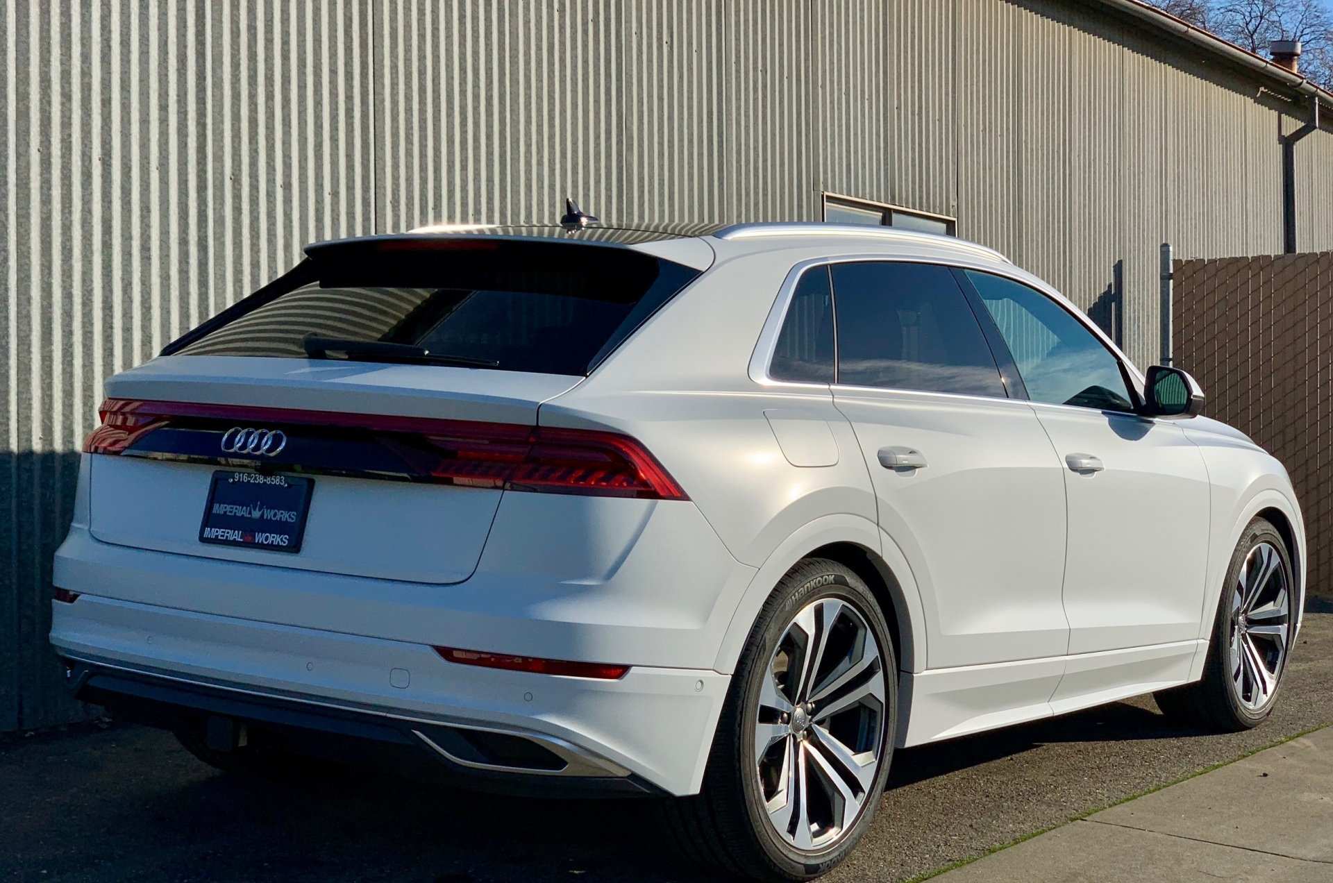 A white audi q8 is parked in front of a building.