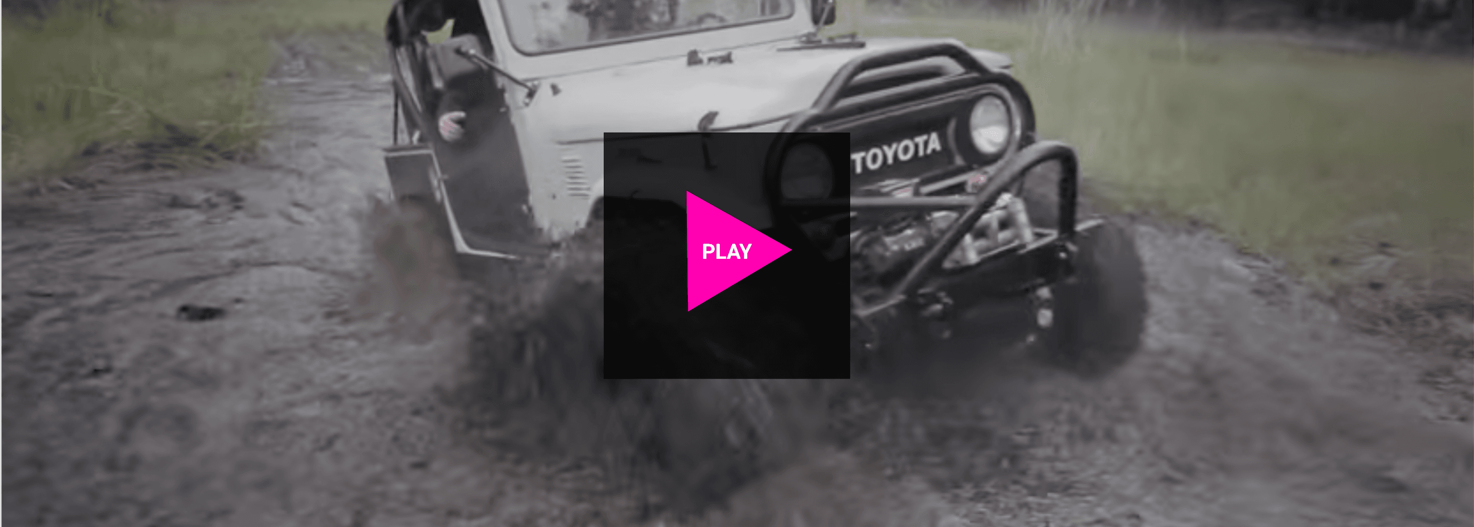 A white jeep is driving through the mud on a dirt road.