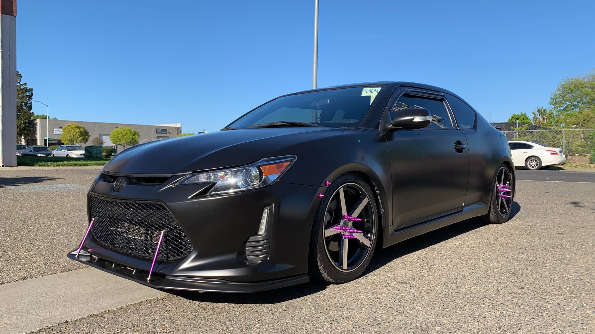 A black car with pink wheels is parked on the side of the road.