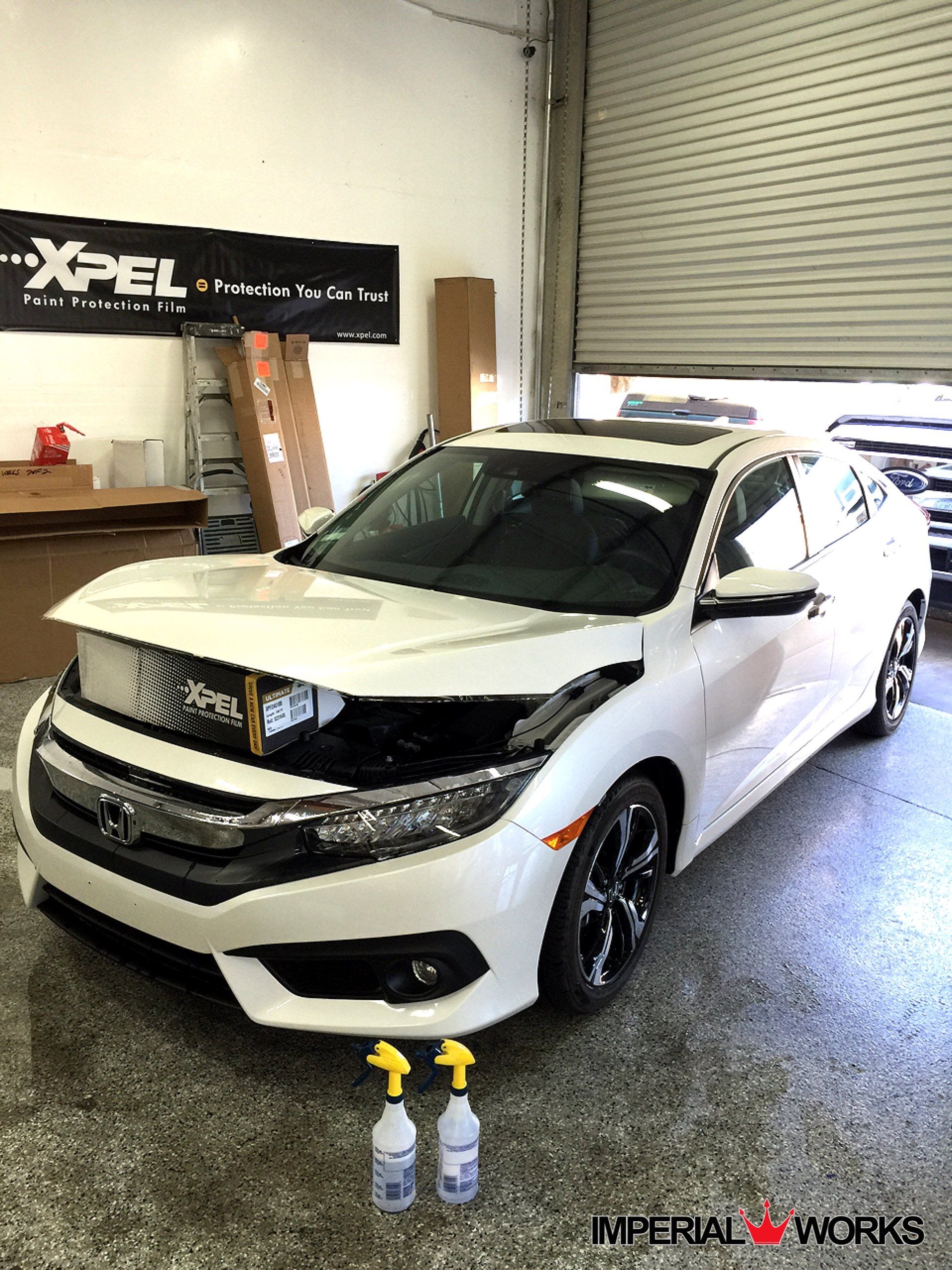 A white honda civic is parked in a garage next to two spray bottles.