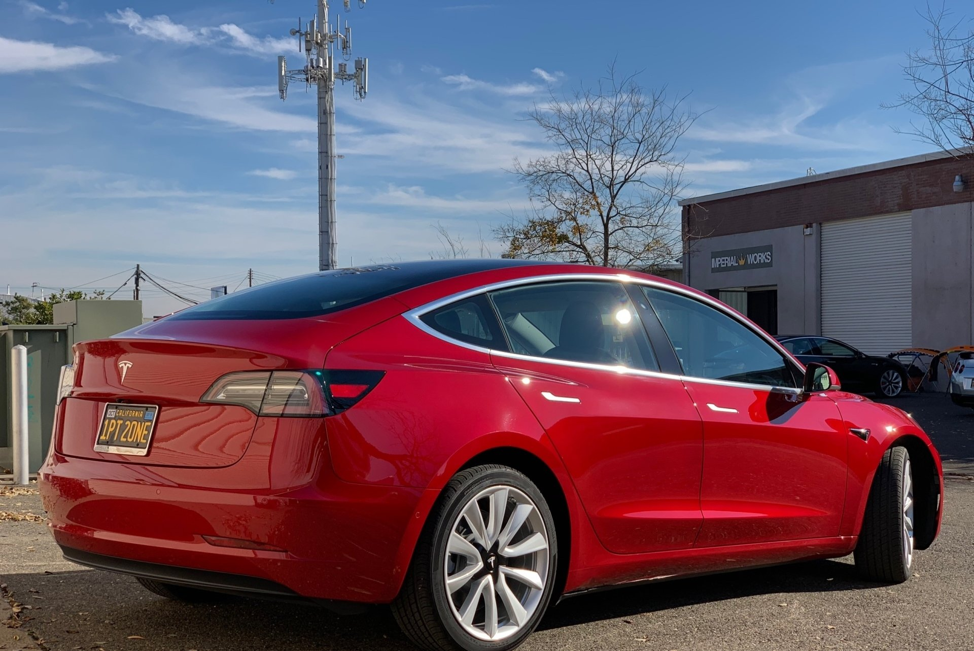 A red tesla model 3 is parked in front of a building.