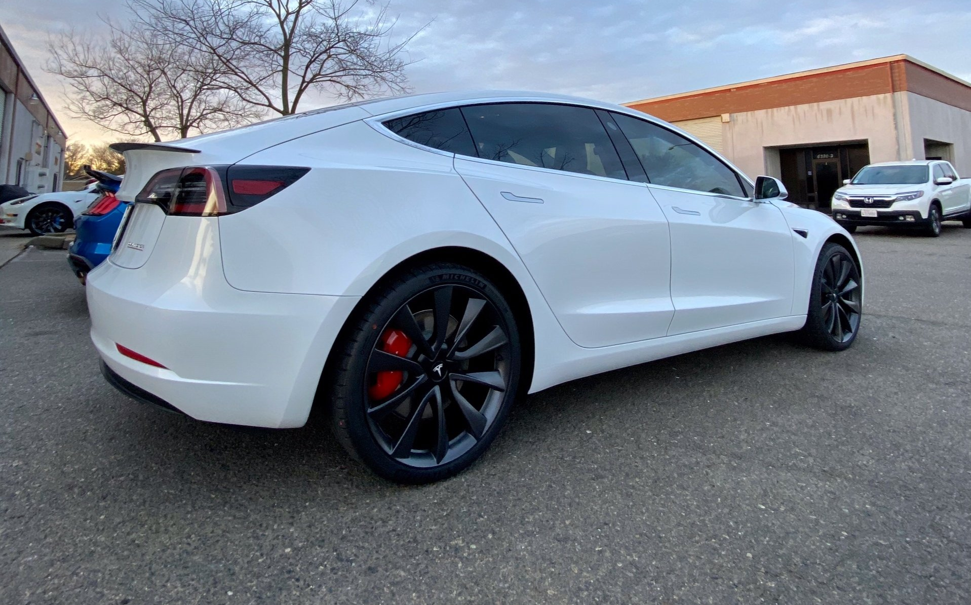 A white tesla model 3 is parked in a parking lot.