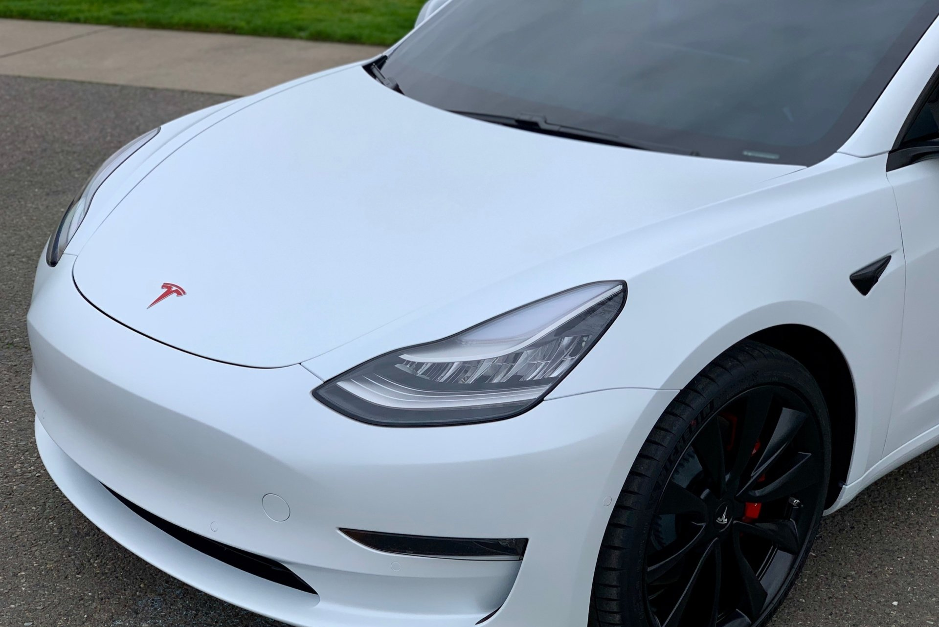 A white tesla model 3 is parked on the side of the road.