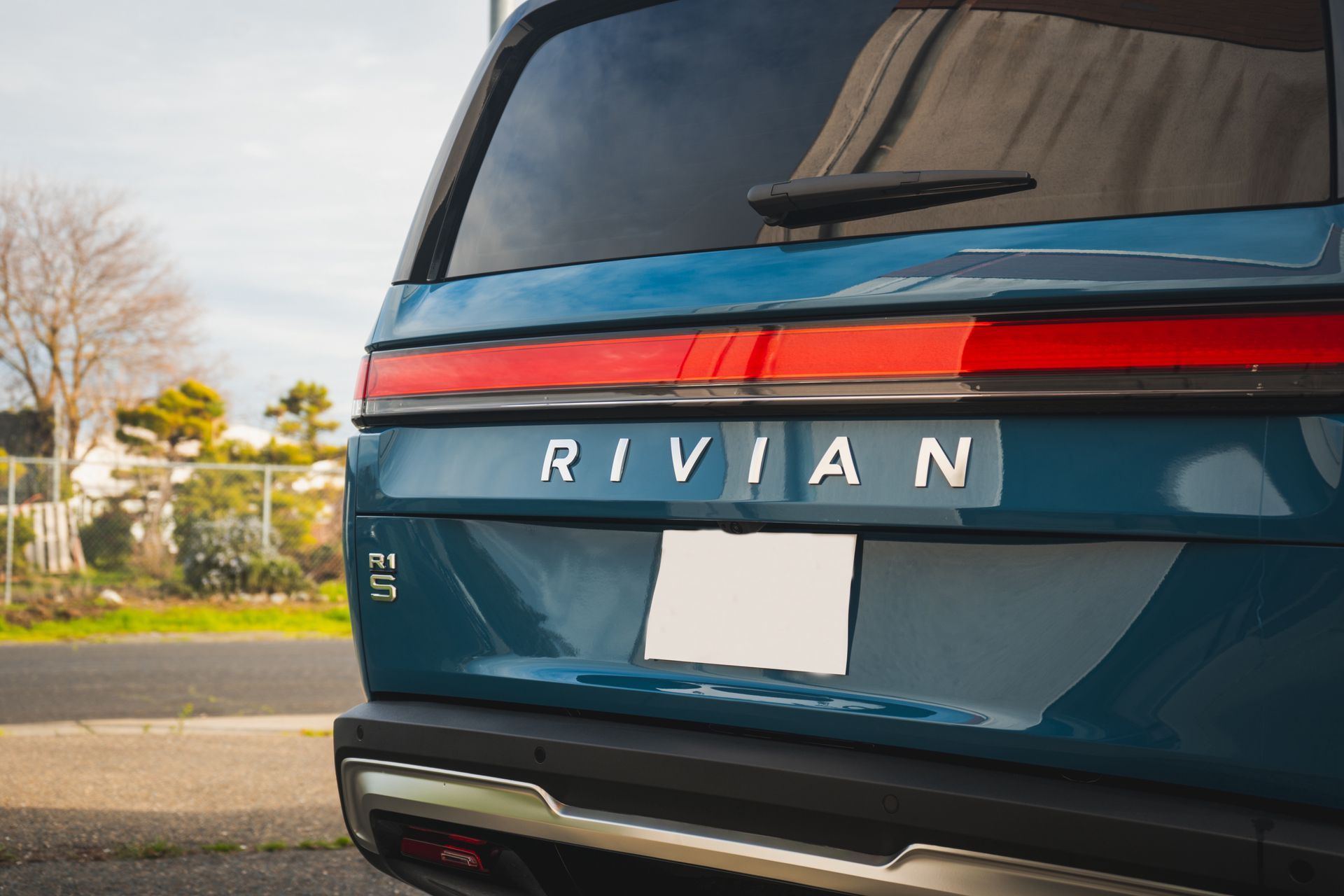 The back of a blue rivian suv is parked on the side of the road.