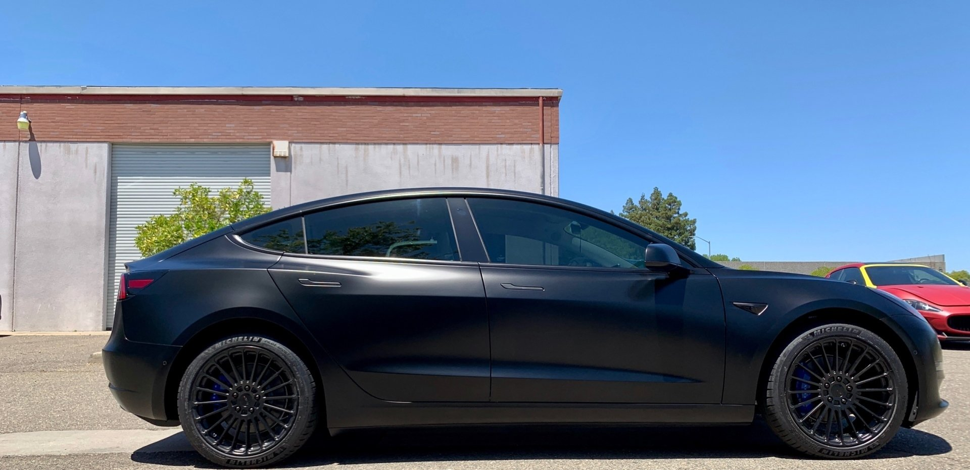 A black tesla model 3 is parked in front of a building.