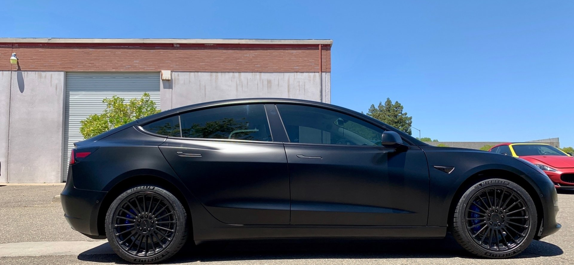 A black tesla model 3 is parked in front of a building.