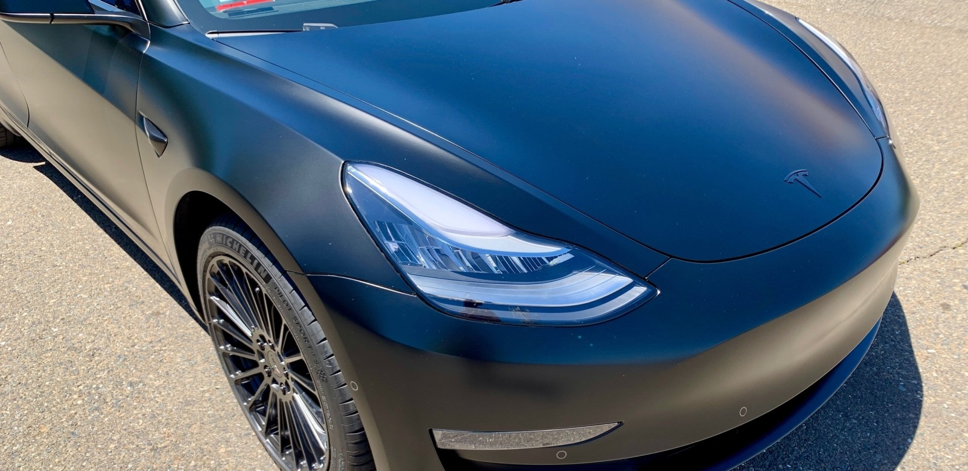 A black tesla model 3 is parked on the side of the road.