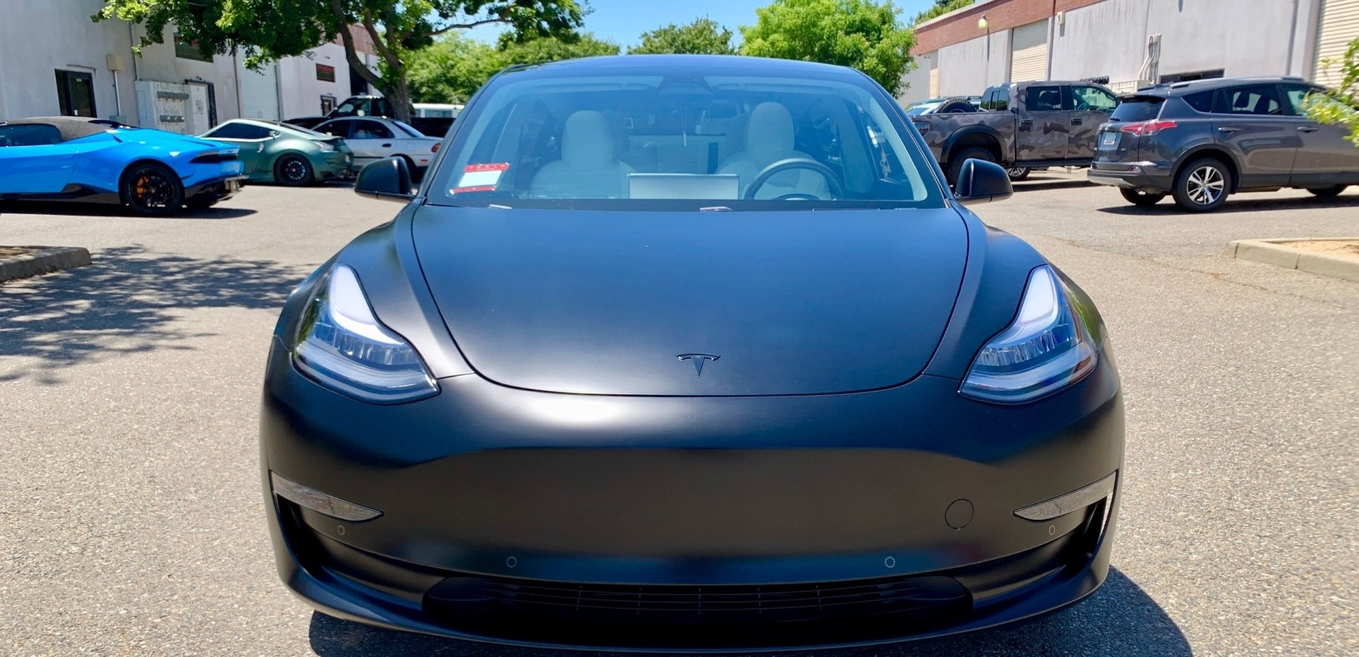 A black tesla model 3 is parked in a parking lot.