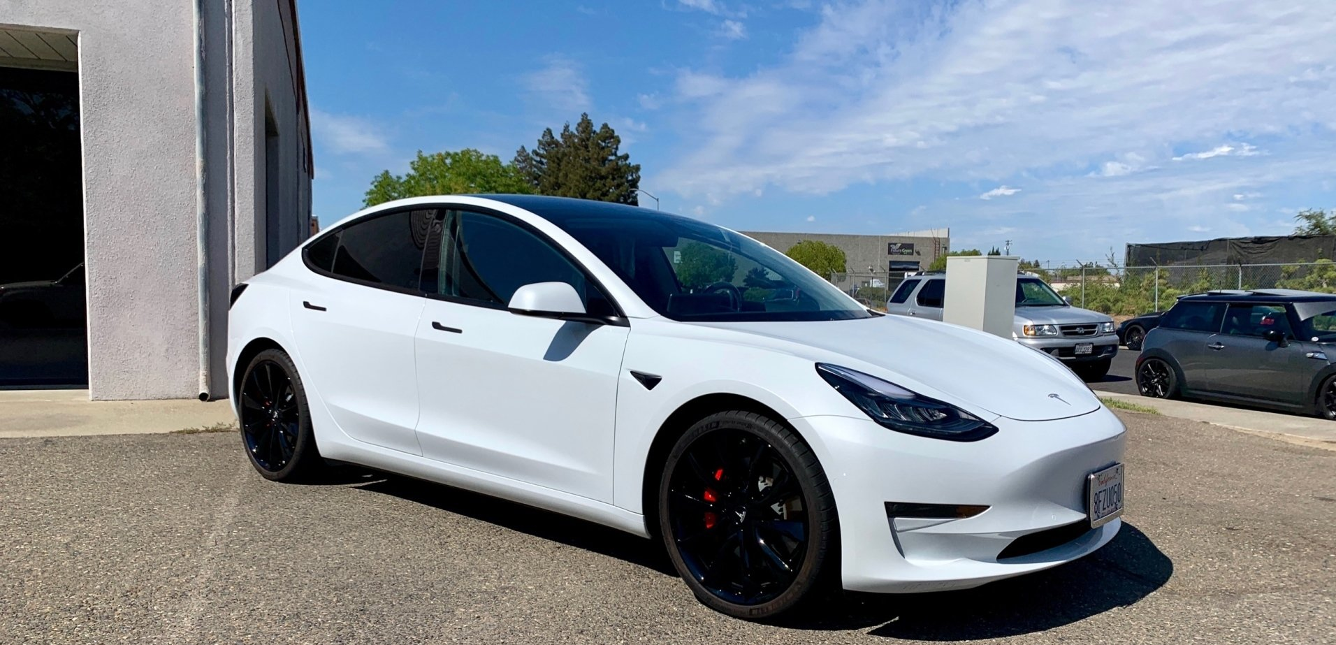 A white tesla model 3 is parked in front of a building.