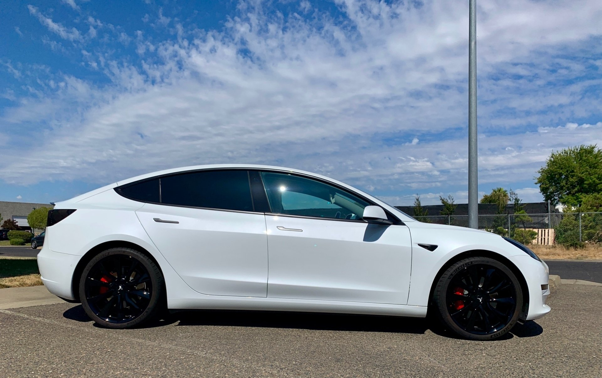 A white tesla model 3 is parked on the side of the road.