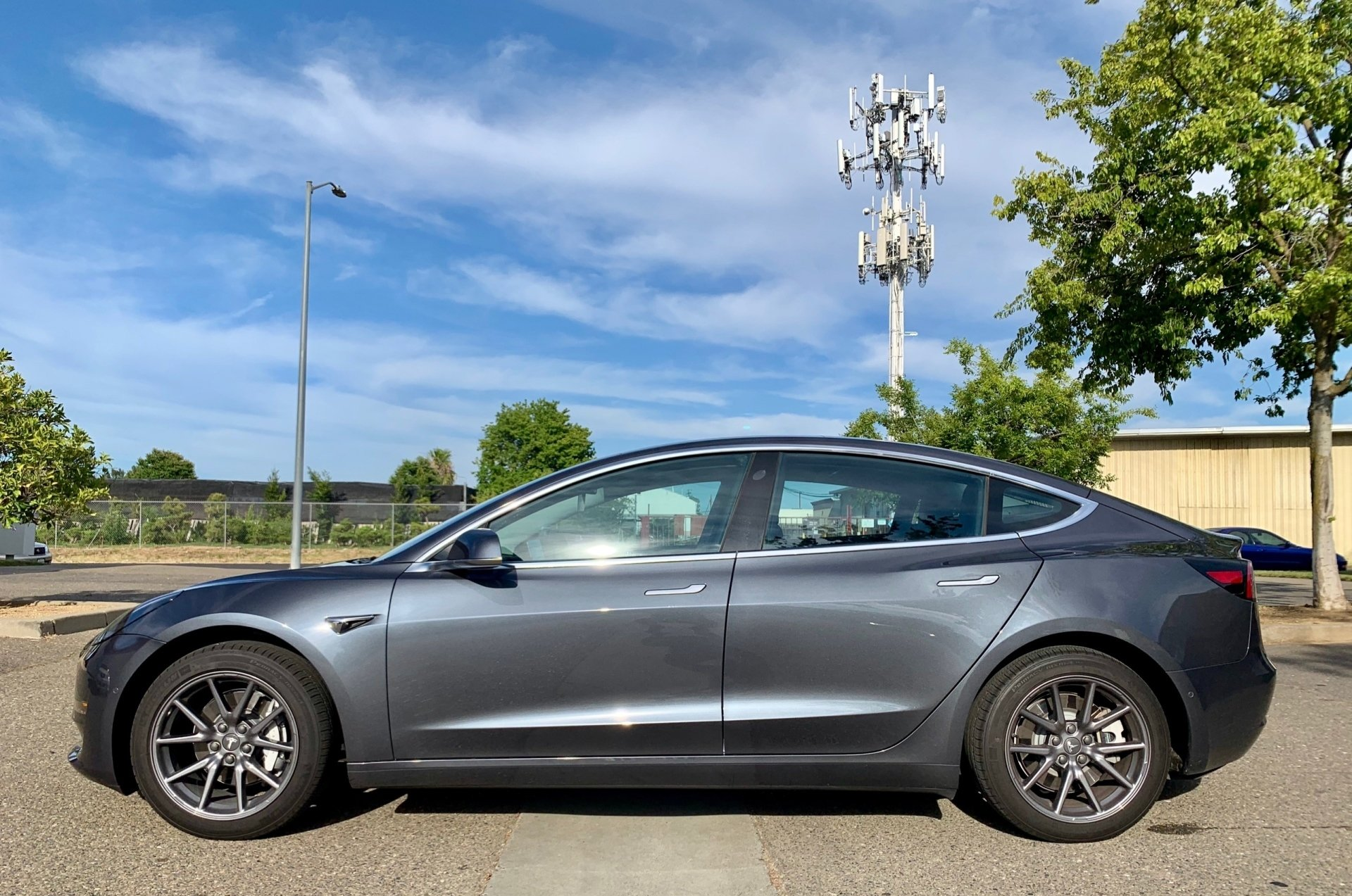 A gray tesla model 3 is parked in a parking lot.