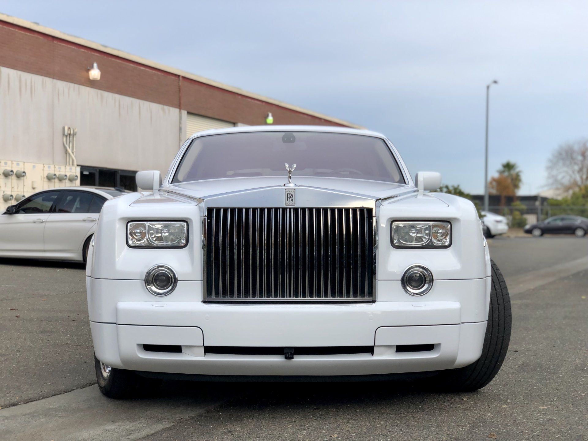 A white rolls royce phantom is parked in front of a building.