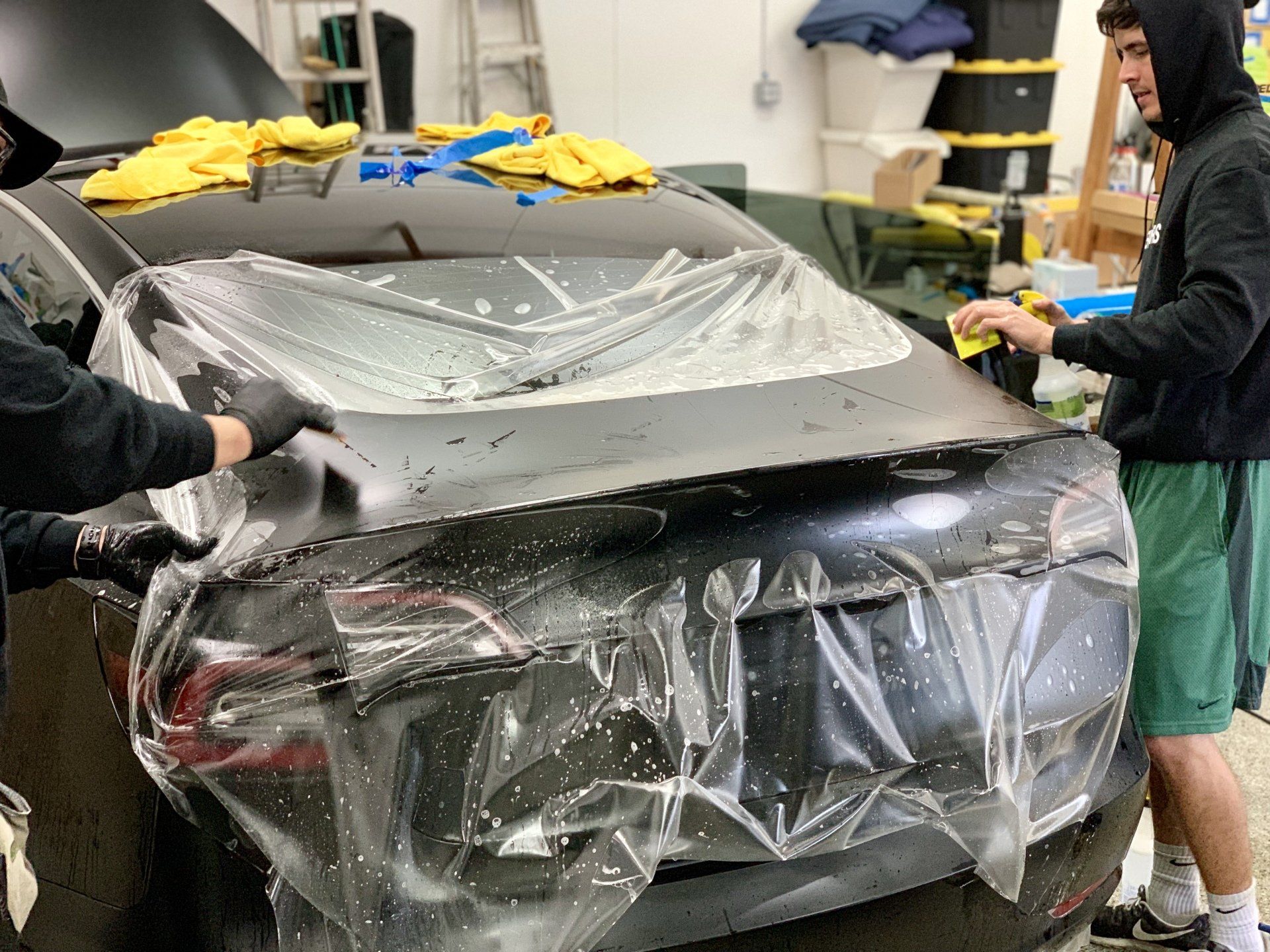 A man is wrapping a car in plastic in a garage.