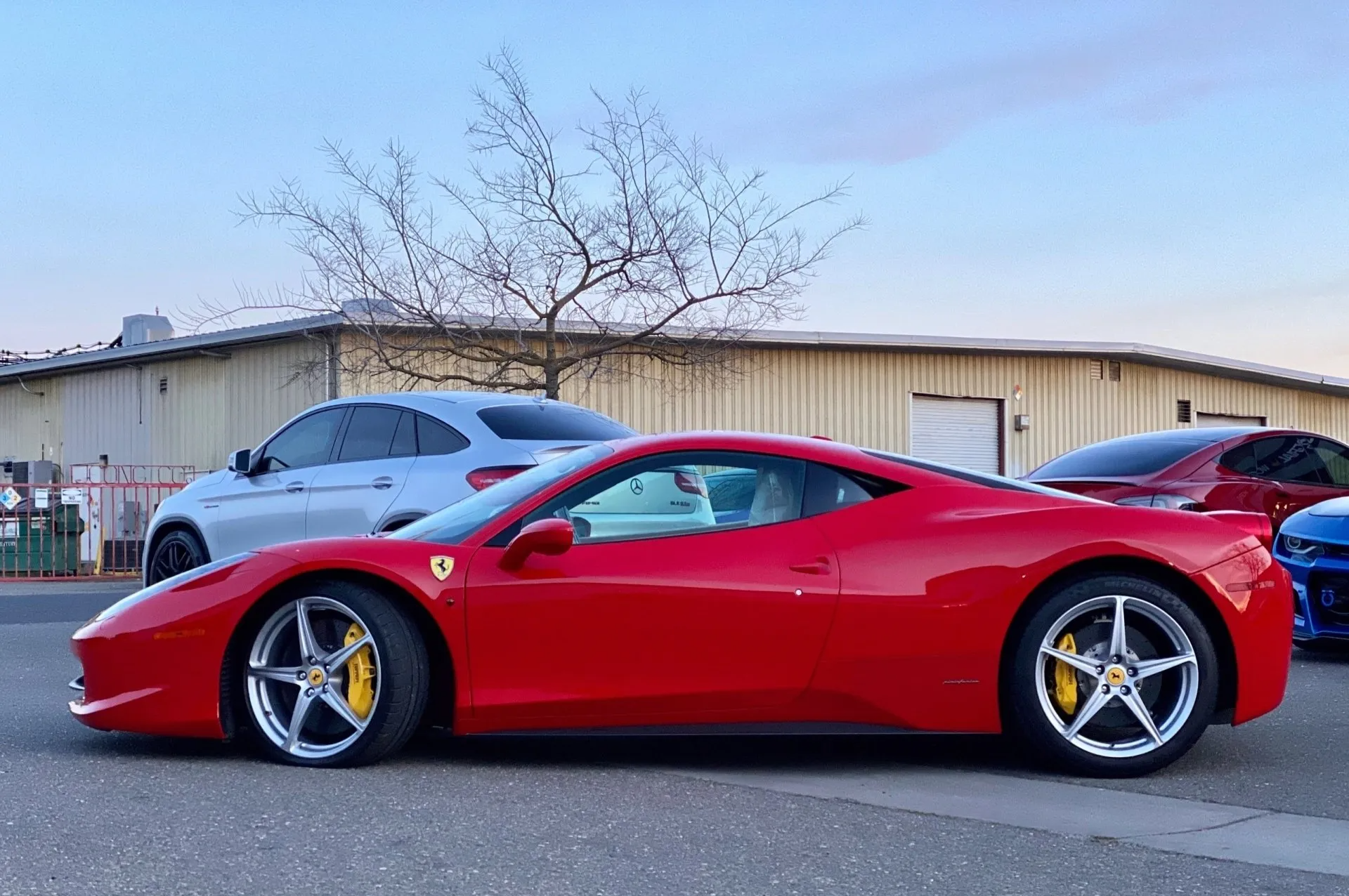 A red ferrari is parked next to a silver car and a blue car.