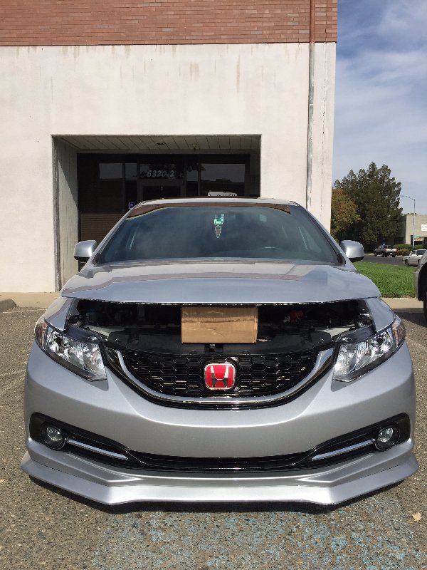 A silver car with the hood up is parked in front of a building with clear bra paint protection