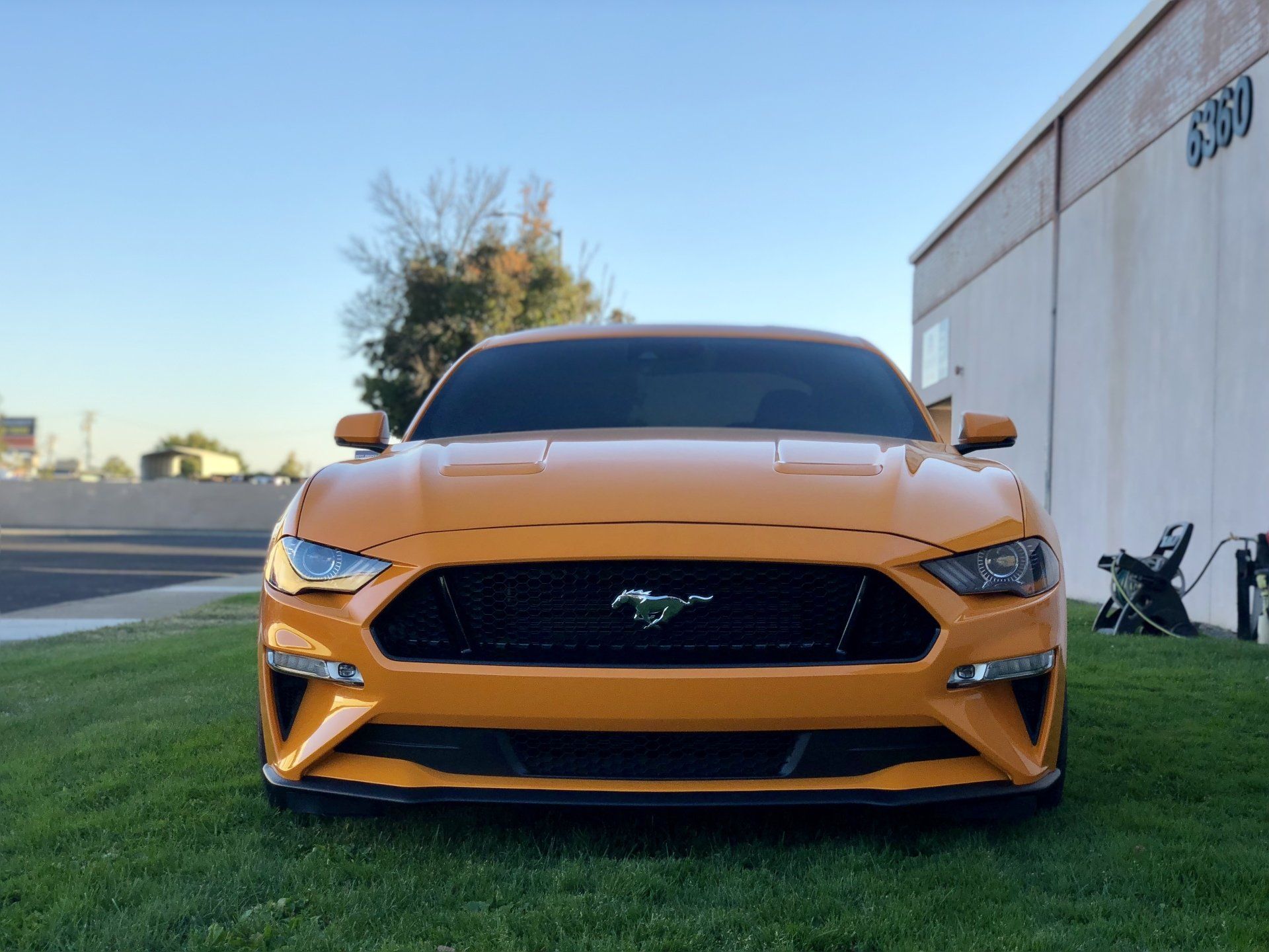 A yellow mustang is parked in the grass in front of a building.