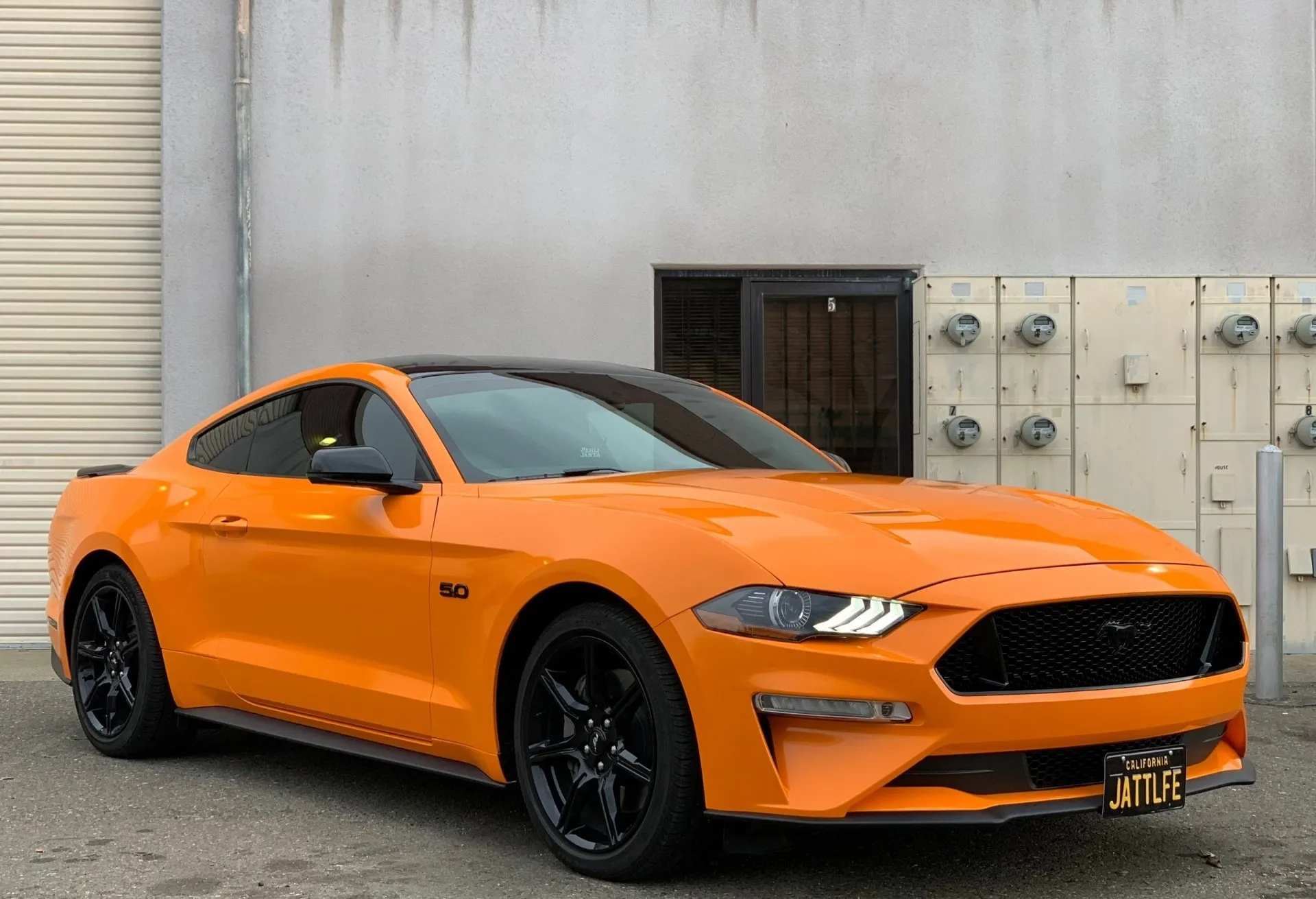 An orange ford mustang is parked in front of a building.