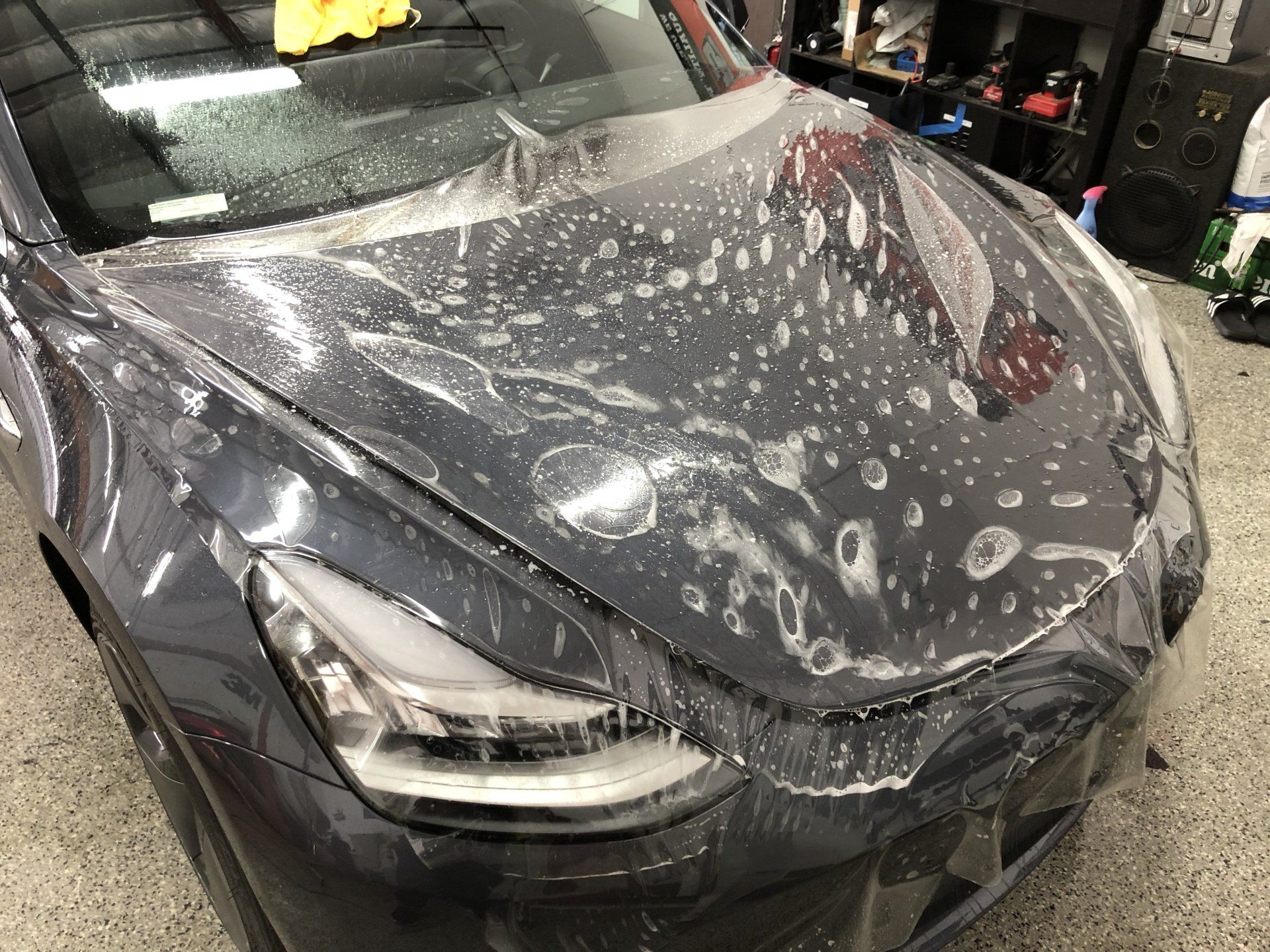 A tesla model 3 is covered in plastic wrap in a garage.