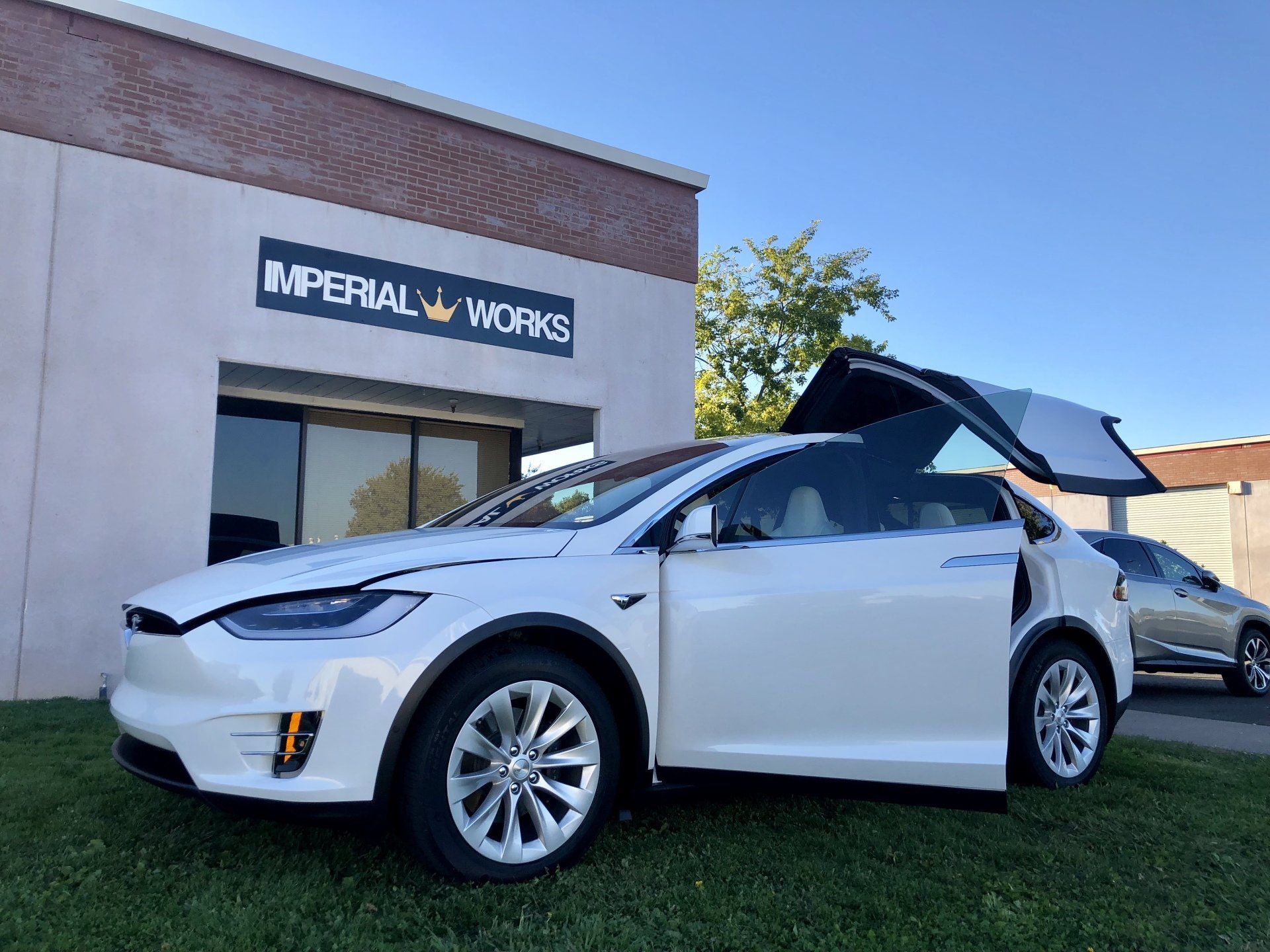 A white tesla model x is parked in front of a building with its trunk open.