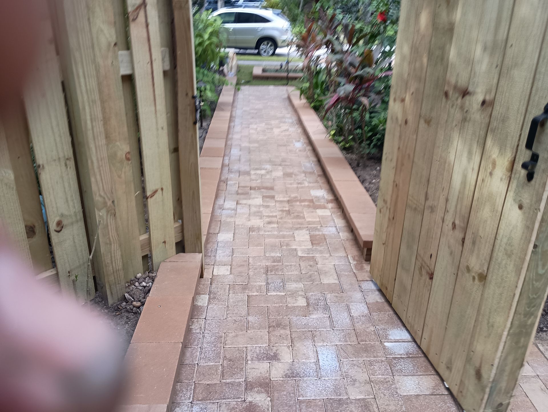 Brick pathway between wooden fences, gate open.