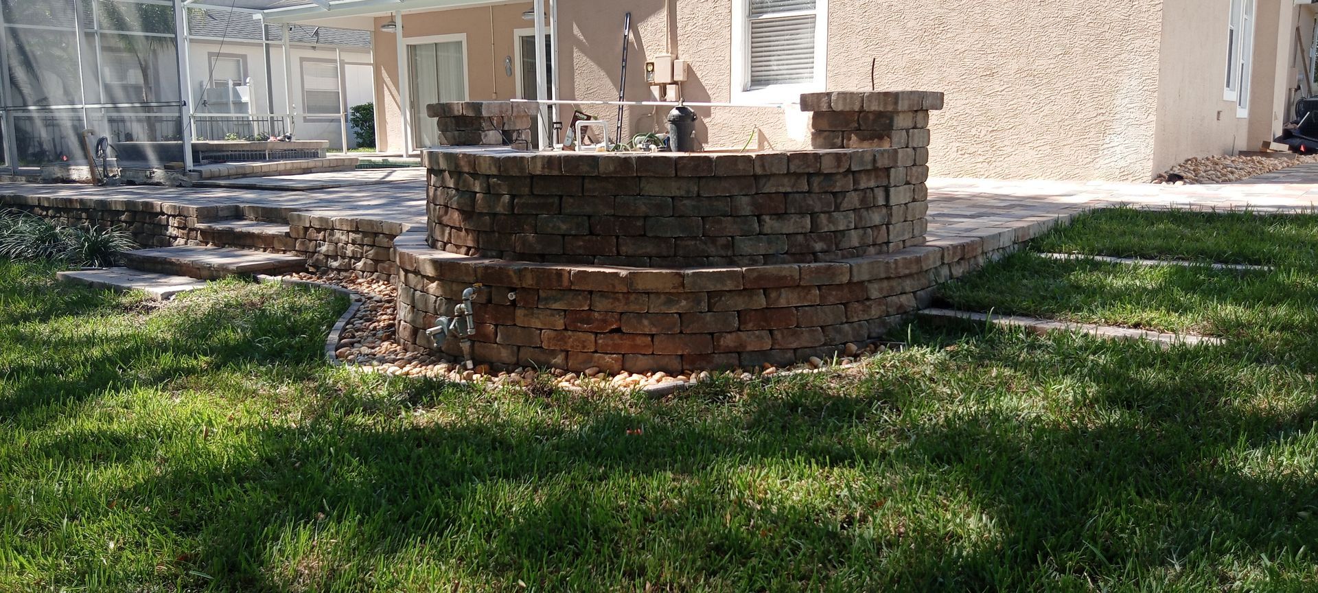 Brick-lined tiered landscaping in a yard with green grass and a house in the background.