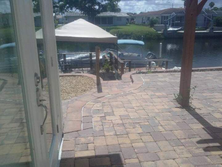Patio with brick pavers leading to a dock and boat under a tan canopy.