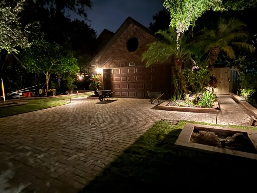 Night view of a brick house with a lit driveway and garden, illuminated by spotlights.