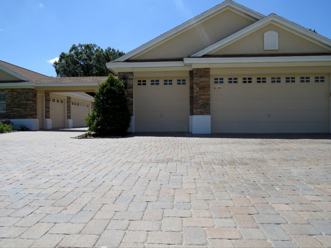 Paver driveway leading to a house with three garage doors and a carport.