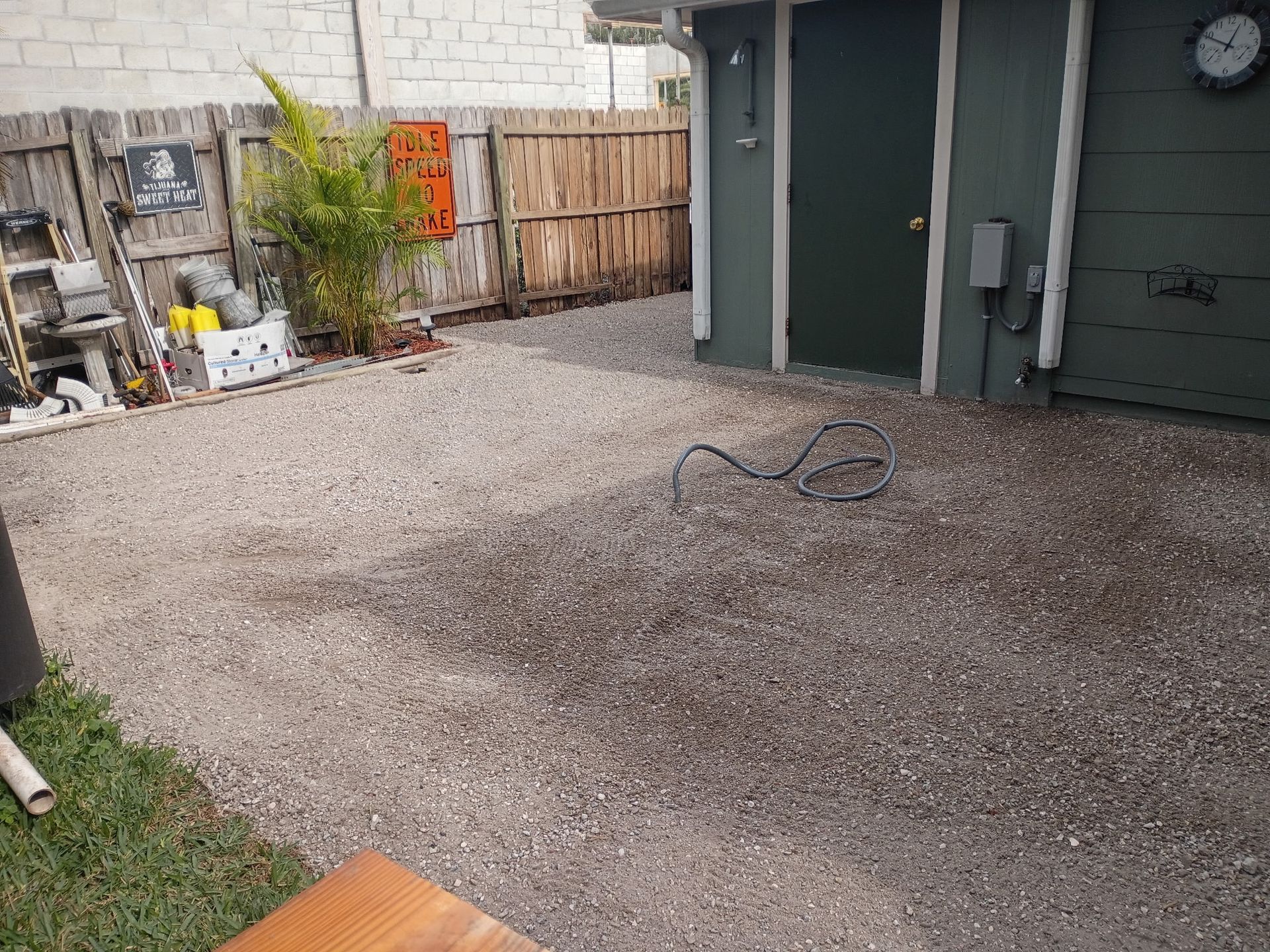 Gravel backyard with a shed, wooden fence, and miscellaneous items.