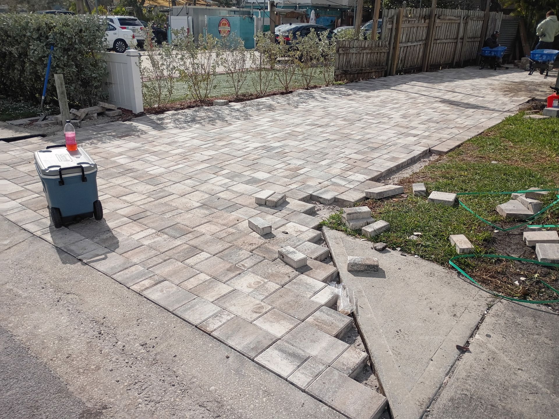 Brick driveway construction with uneven edge next to a concrete sidewalk.