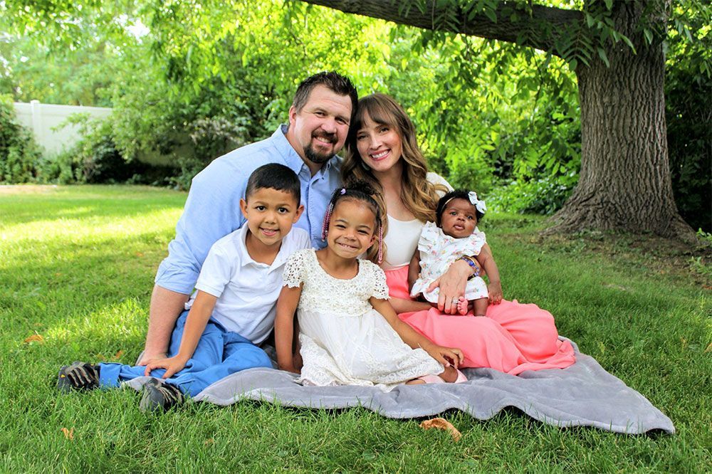 A family is sitting on a blanket in the grass under a tree. A family is sitting on a blanket in the grass under a tree.