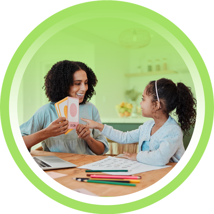 A caregiver smiling while supporting a young girl during an at-home learning activity