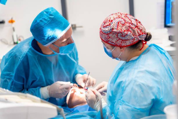 Oral surgeon and surgical assistant performing a dental procedure on a patient in a sterile clinical setting.