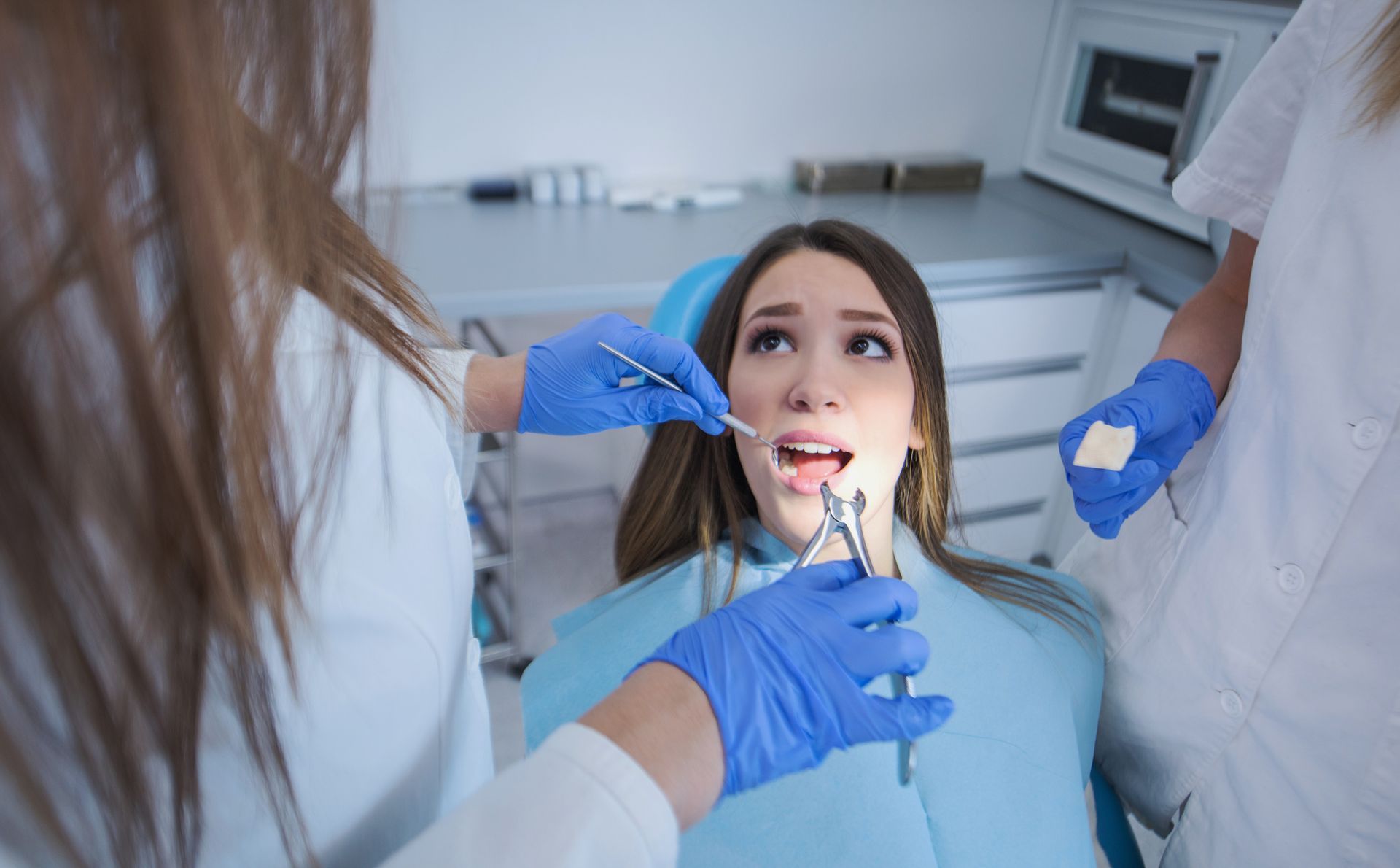 Brunette woman getting her wisdom tooth removed by two focused dentists.
