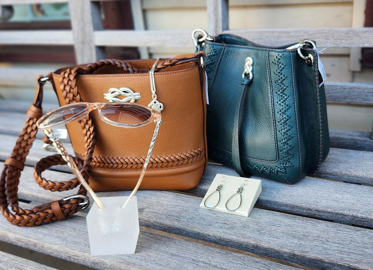 A brown purse and a green purse are on a wooden bench